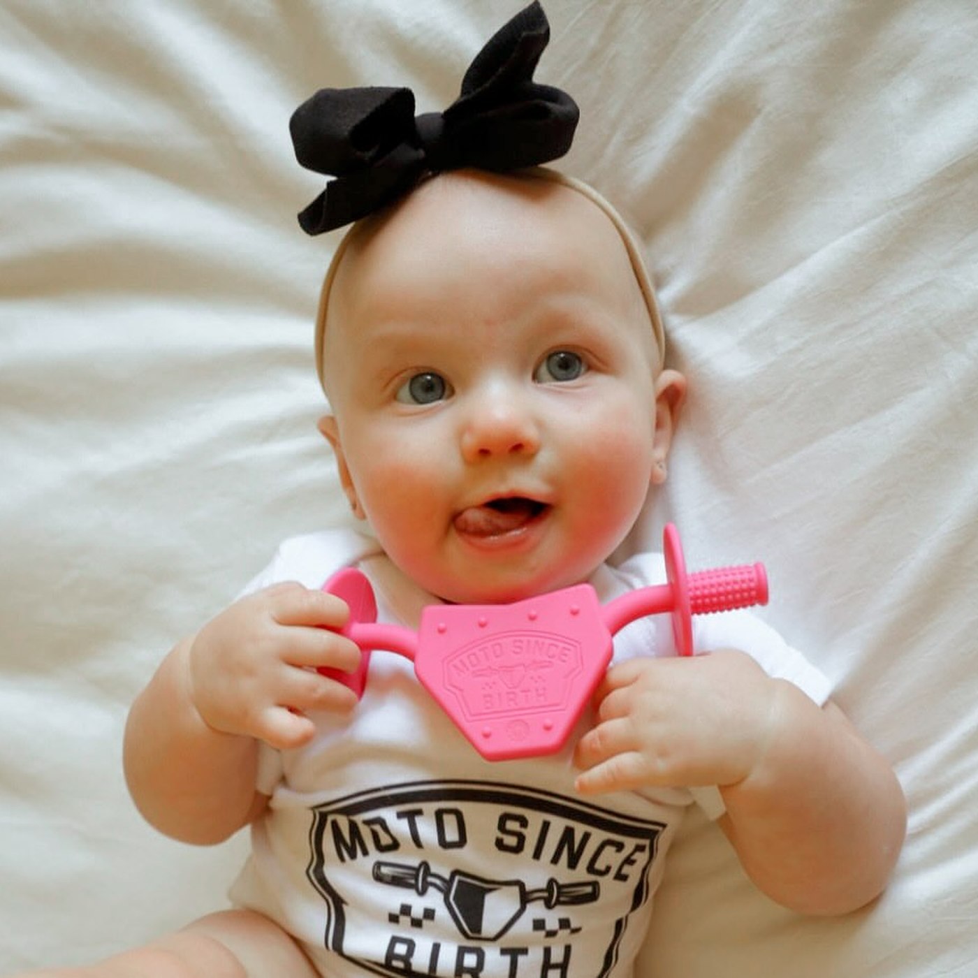 Baby in a Moto Since Birth bodysuit holding the pink motocross teether