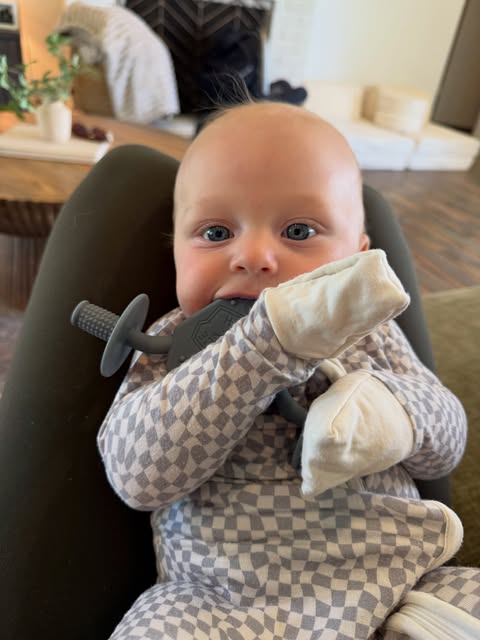 Baby chewing a Moto Since Birth teether wrapped in a checkered blanket