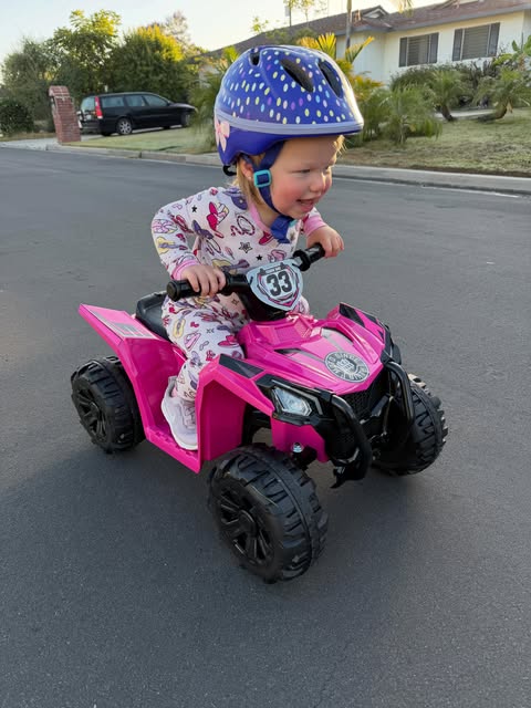 Toddler in a helmet riding a pink quad