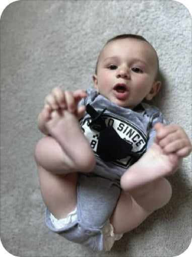 Baby in a grey Moto Since Birth bodysuit lying on a cream rug